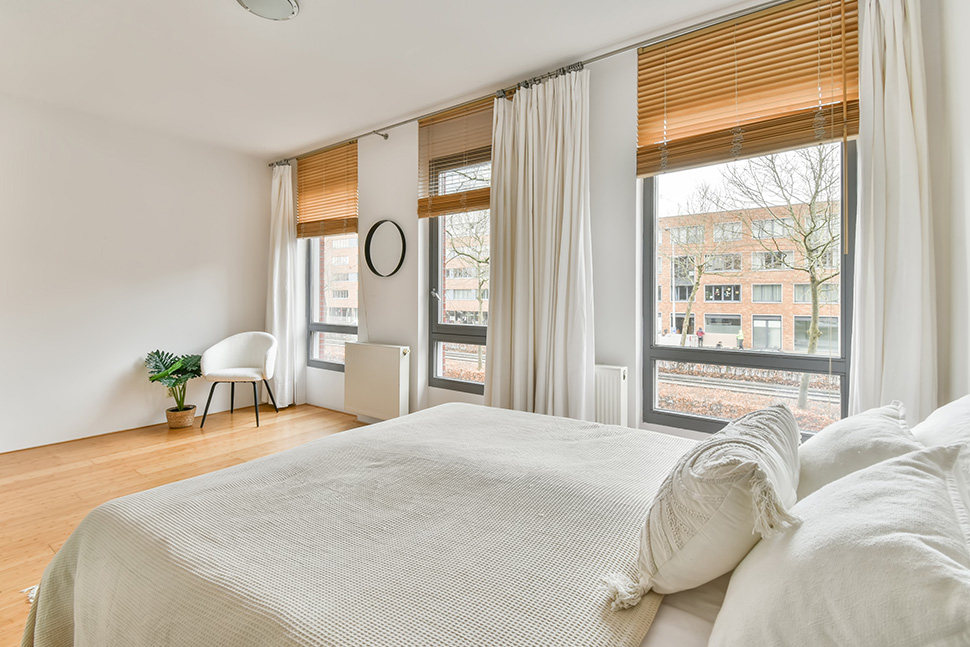 Helles, modernes Schlafzimmer mit einer Kombination von Raffrollos und weissen, langen Vorhängen